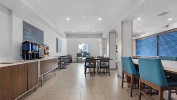 Una cafetería moderna, bien iluminada, con una barra larga, varias mesas y sillas.