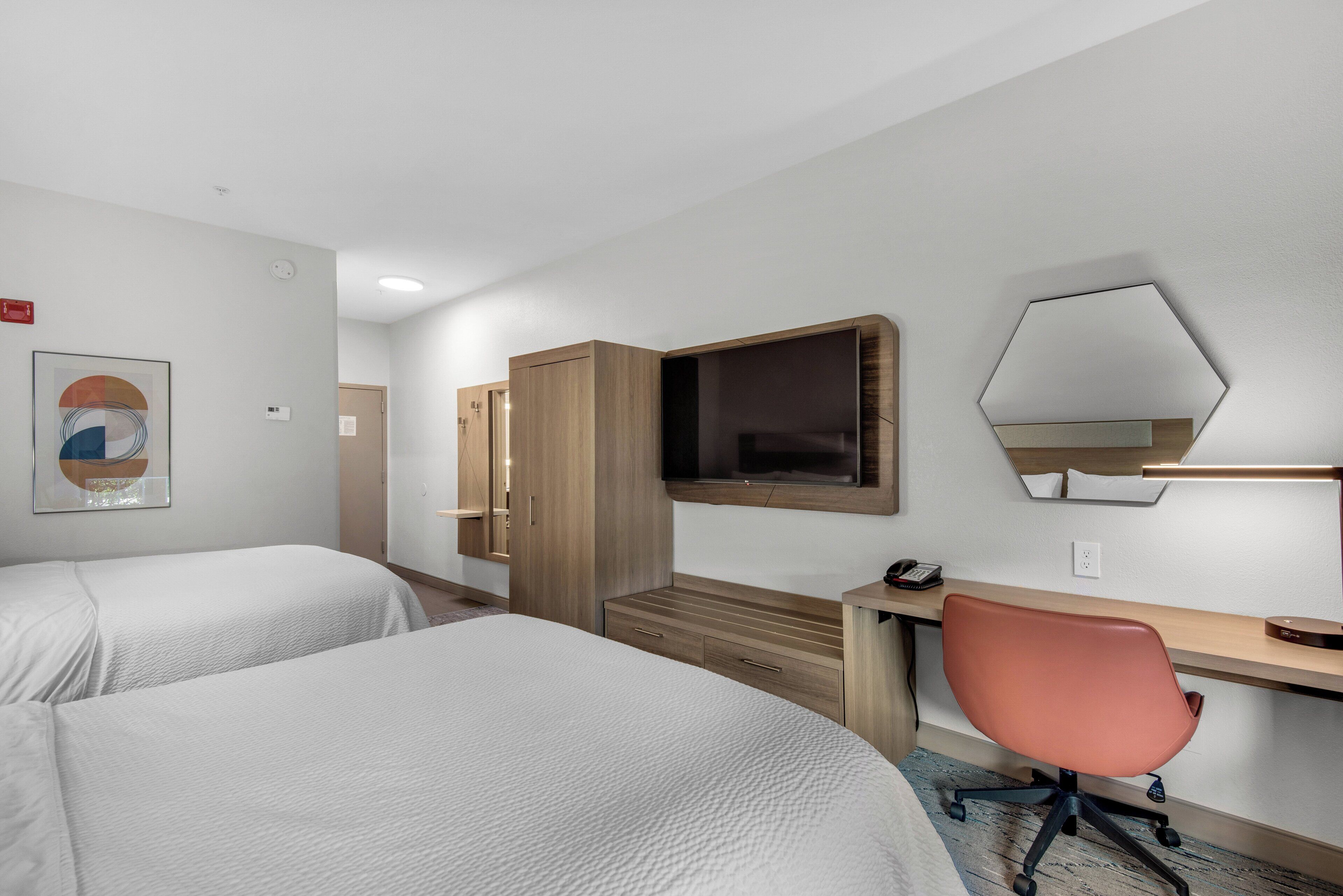 Una habitación de hotel con dos camas, un escritorio con silla, un televisor y un espejo.