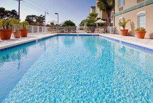 Una piscina cristalina con borde de azulejos, rodeada por una cerca blanca y plantas en macetas.