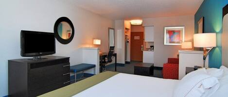 Habitación de hotel con cama, escritorio con televisor, una silla y lámpara de escritorio.