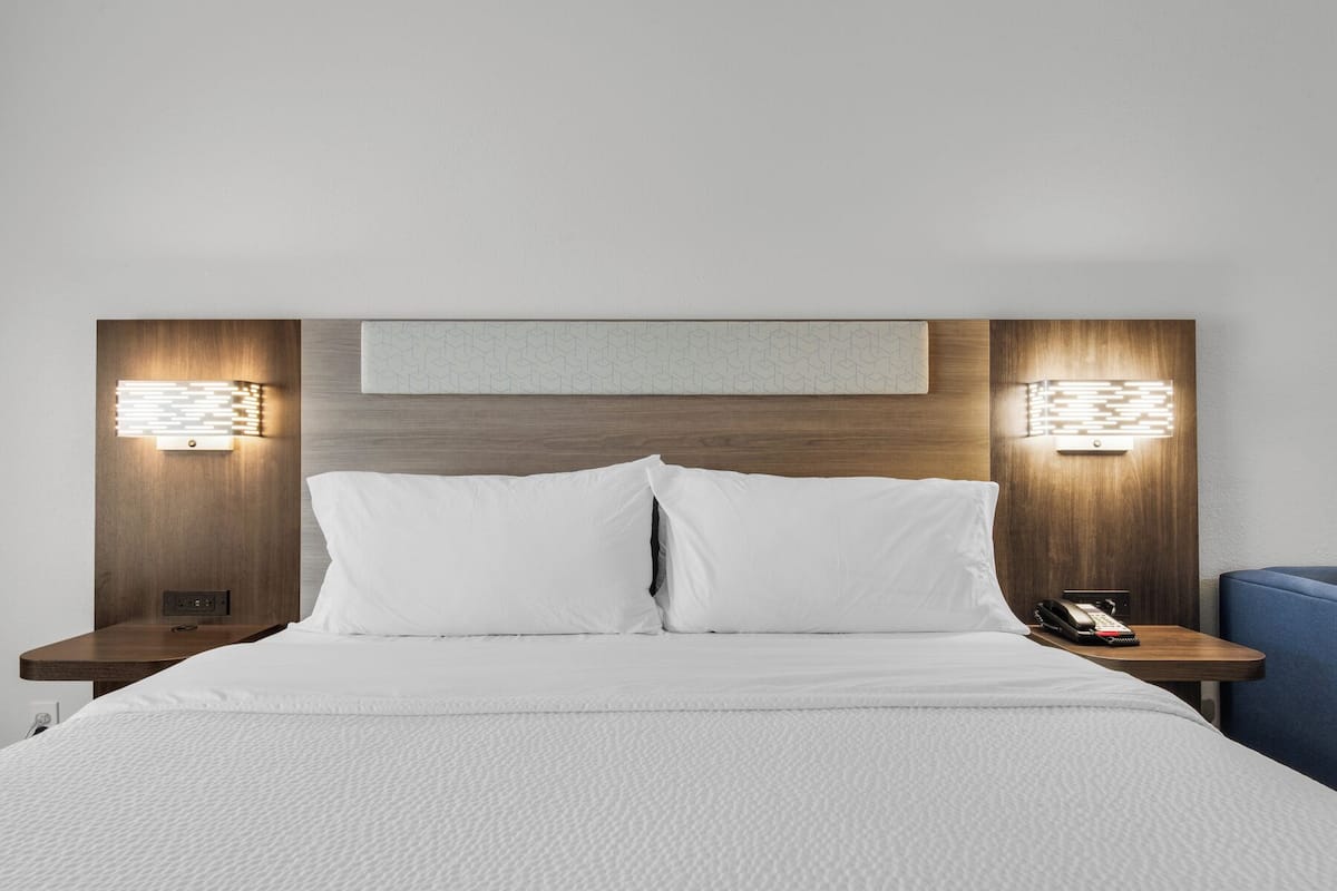 A hotel room with a large bed, two bedside tables with lamps, a phone, and a small blue chair.