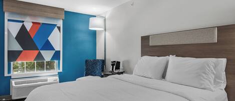 A hotel room with a large bed, a nightstand, a lamp, and a window with a geometric wall art piece.