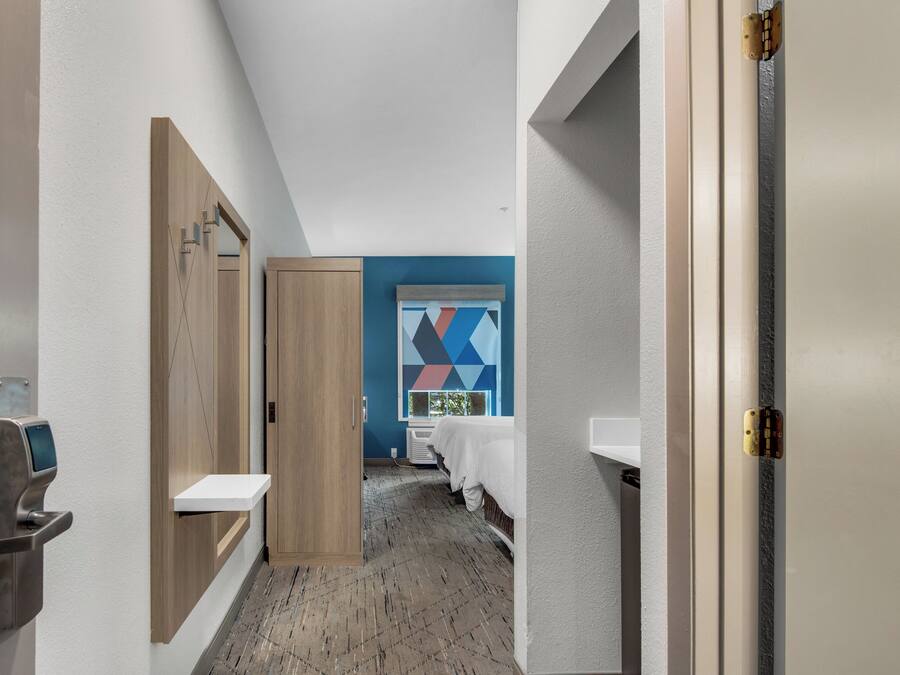 A hotel corridor with a wooden wardrobe, a white sink, and a bed with a blue wall in the background.