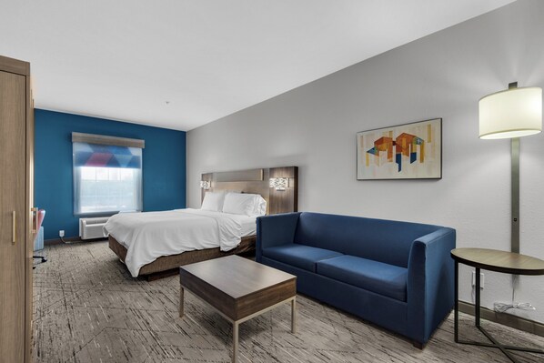 A hotel room with a bed, a blue sofa, a small table, a lamp, and a painting on the wall. - Holiday Inn Express Destin E - Commons Mall area by IHG (Destin)