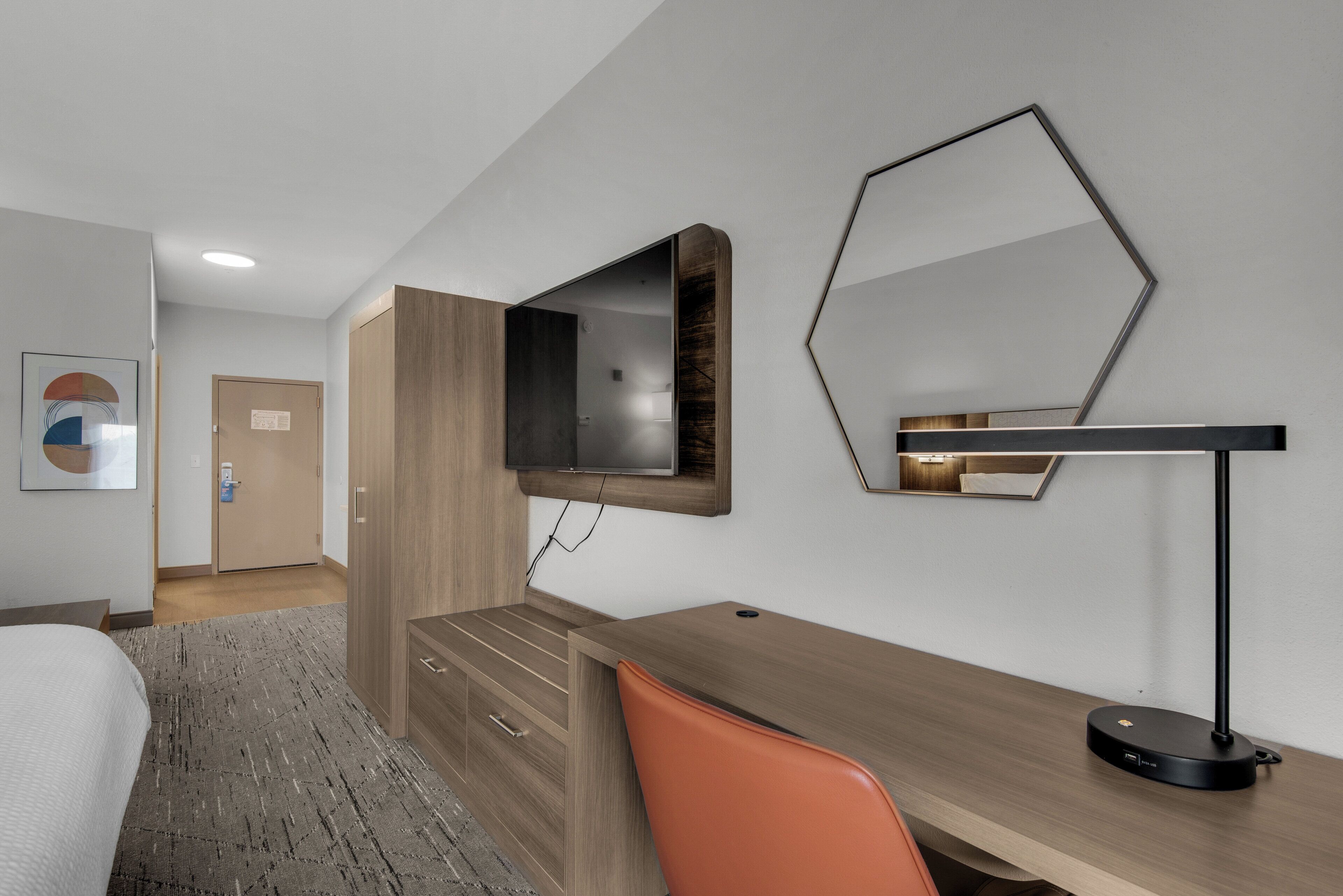 Una habitación de hotel con cama, escritorio, silla, televisor y espejo.