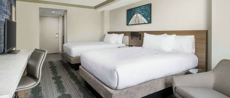 A hotel room with two beds, a desk, a chair, and a TV.