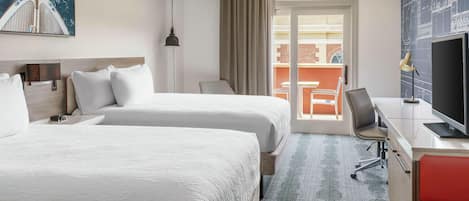 Quarto de hotel com duas camas, uma escrivaninha com televisão, uma cadeira e varanda com vista para a cidade.
