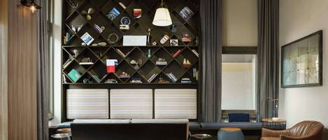 A modern living room with a dark sofa, a round coffee table, a leather armchair, and a wall-mounted bookshelf filled with various items.