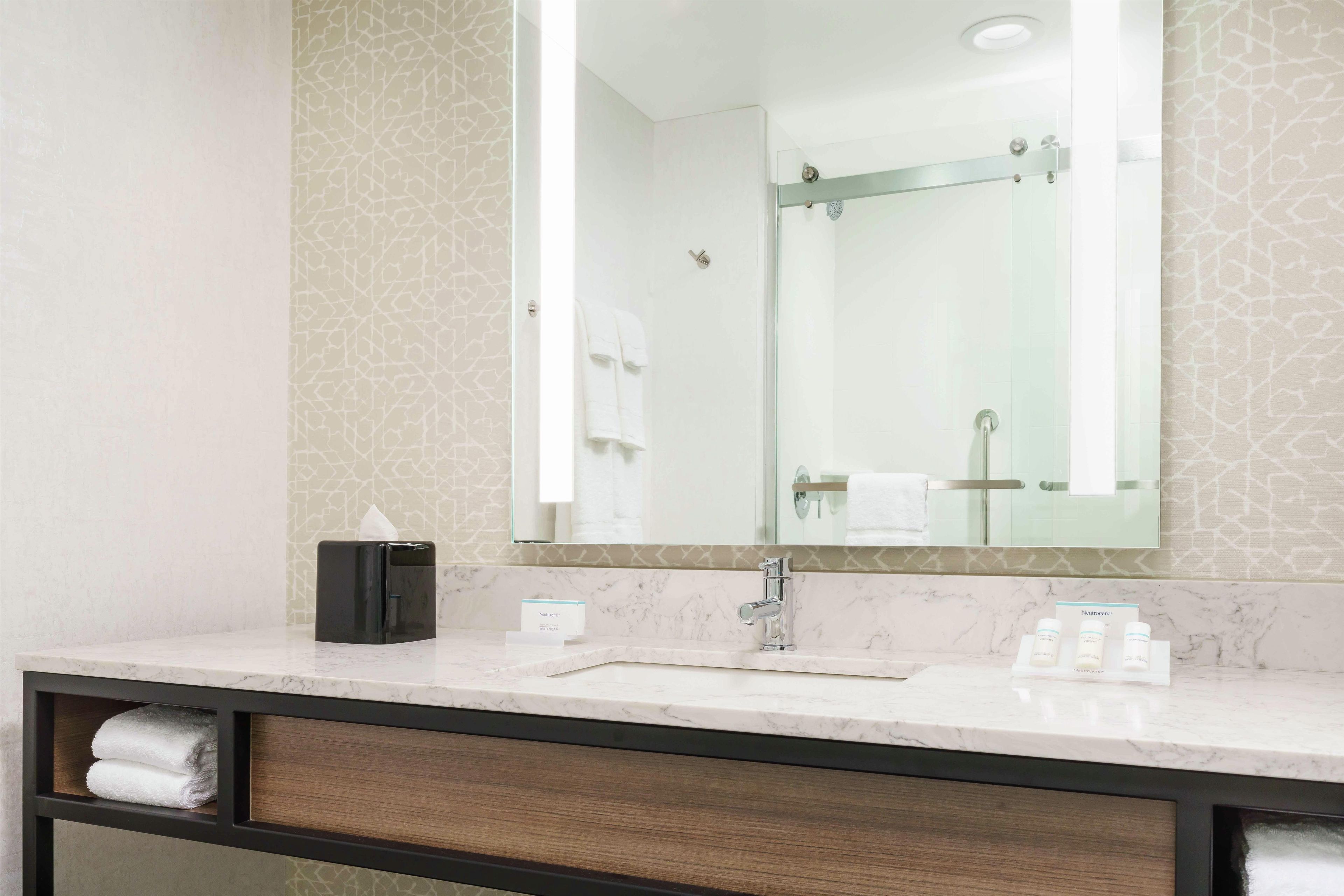 A bathroom with a large mirror, a sink, and a towel rack.