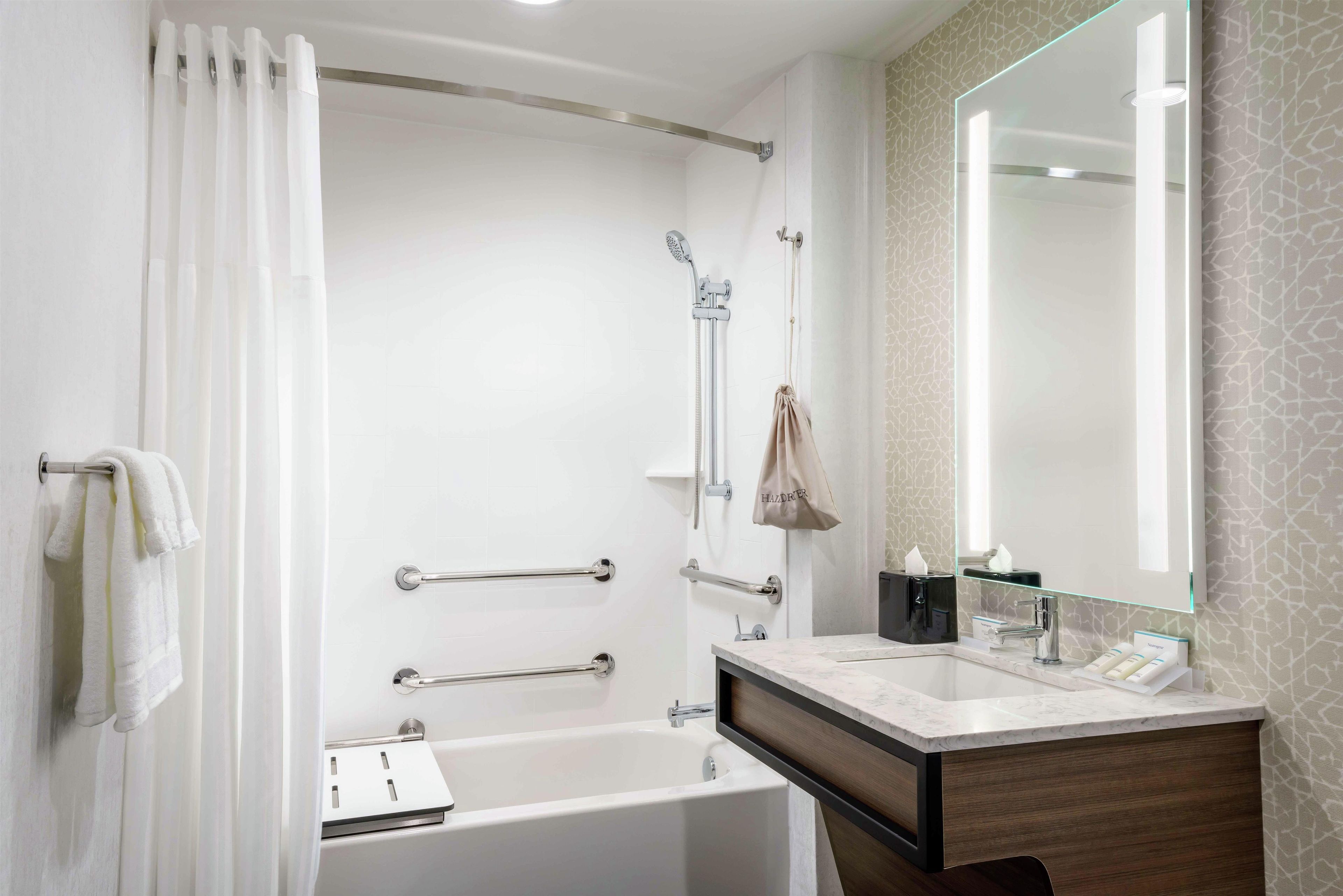 Een moderne badkamer met een bad, een douche, een wastafel met spiegel en een handdoekhouder.