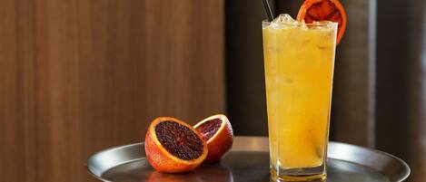 A tall glass of orange juice with a slice of blood orange and a straw, placed on a metal tray.