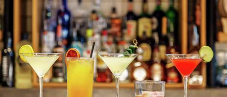 A bar with various cocktails and a selection of bottles in the background.