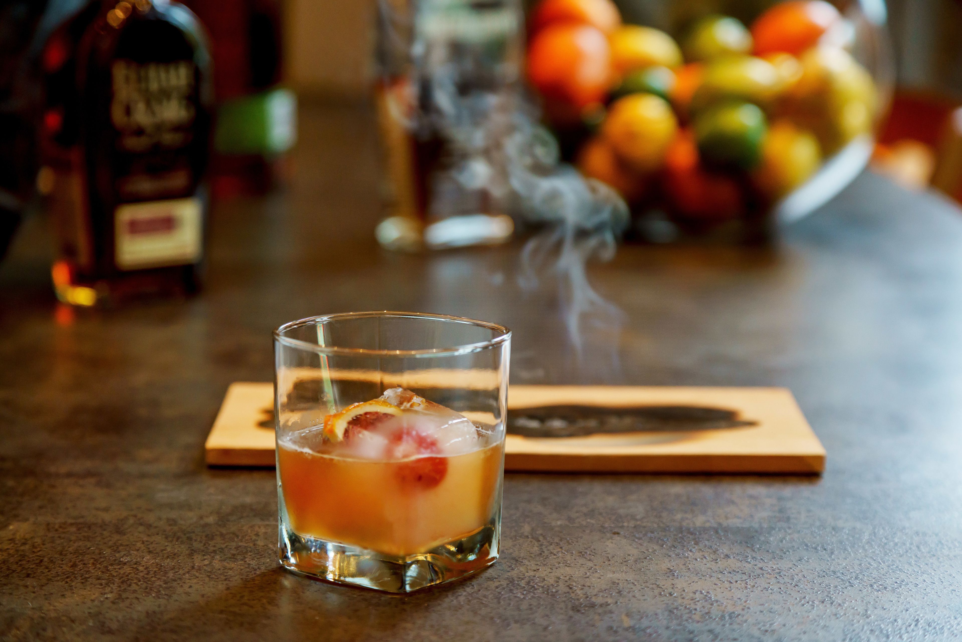 A glass of iced beverage with a slice of fruit on a wooden coaster.
