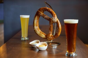 A pretzel on a hook, two small bowls of butter, and two glasses of beer on a wooden table. - Hilton Garden Inn Annapolis Downtown (Annapolis)