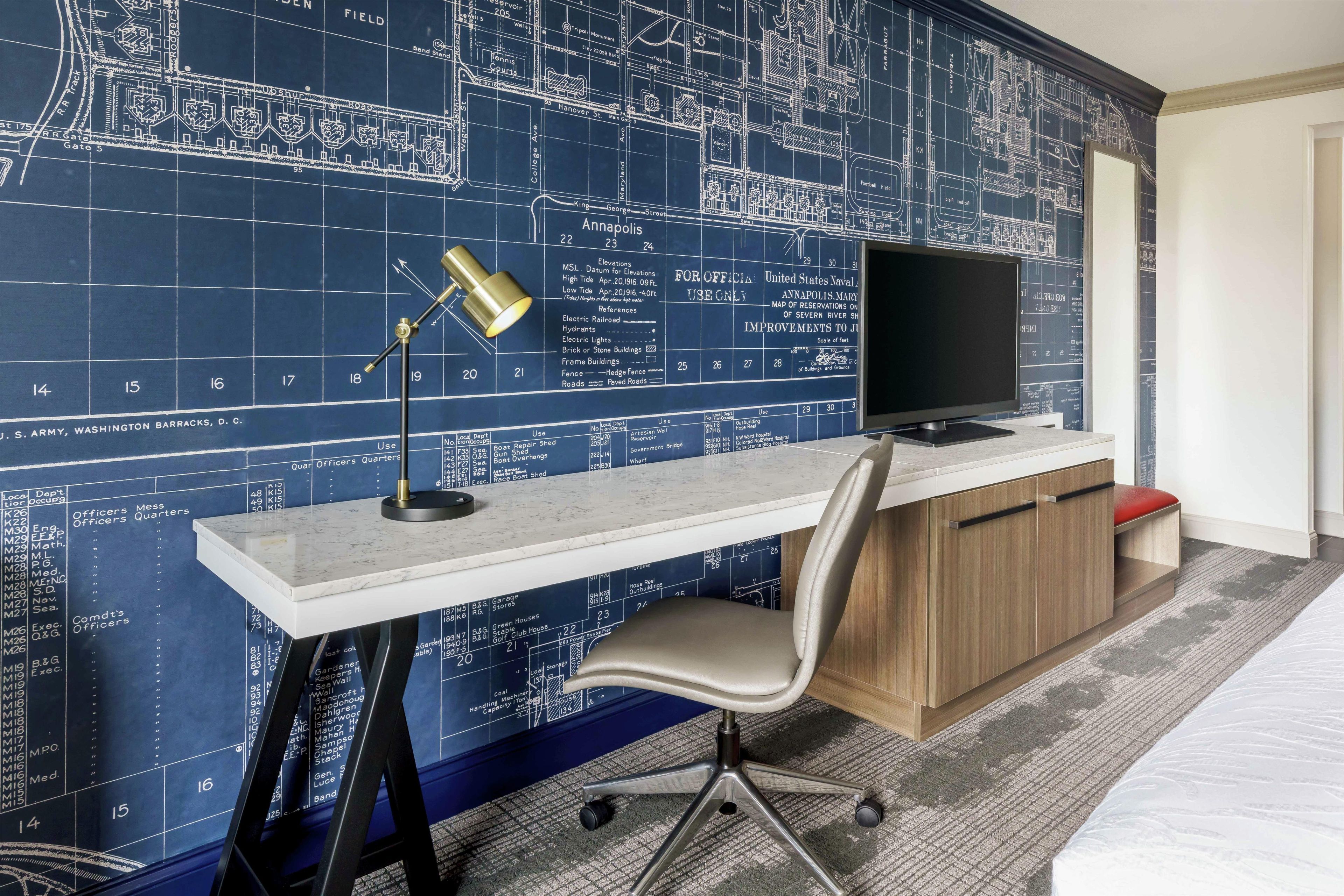 A hotel room with a large map on the wall, a desk with a computer, and a chair.