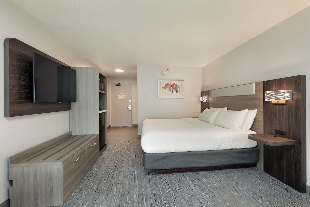 A modern hotel room with a large bed, a flat-screen TV mounted on the wall, a bedside table, and a built-in wardrobe.