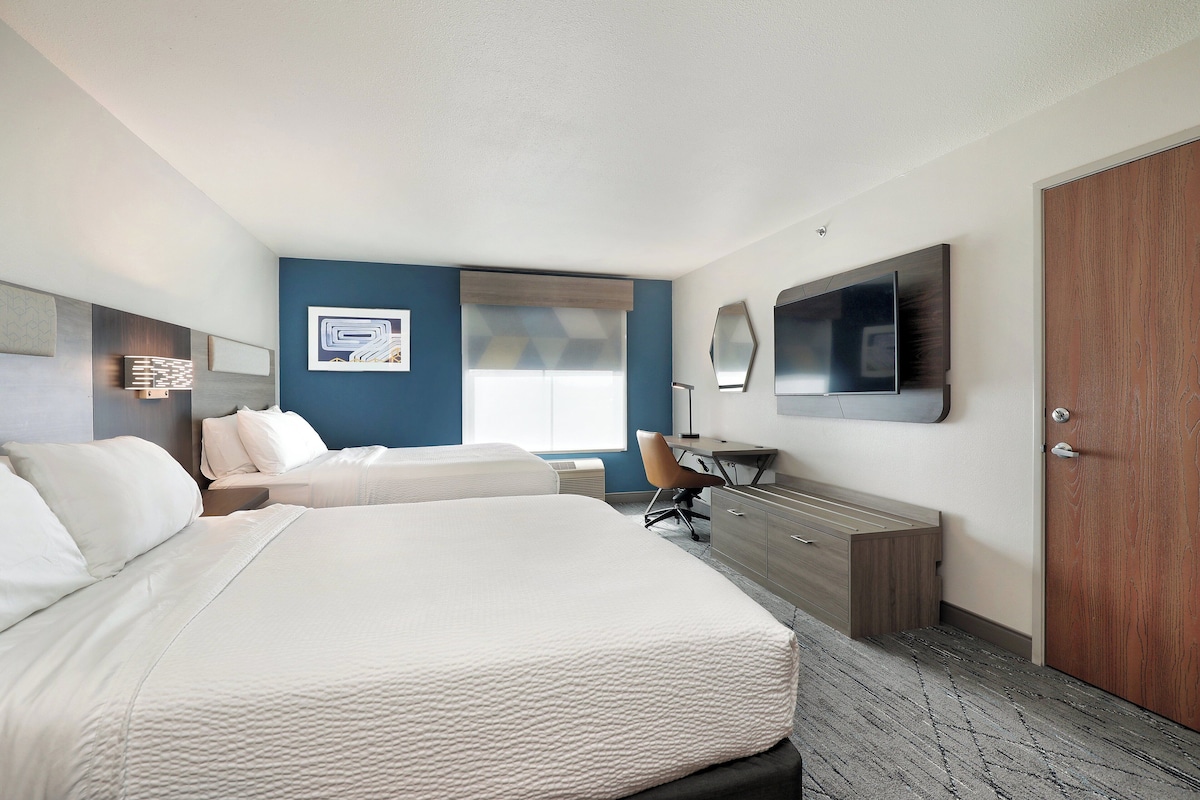 A hotel room with a large bed, a desk, a chair, a wardrobe, and a television on the wall.