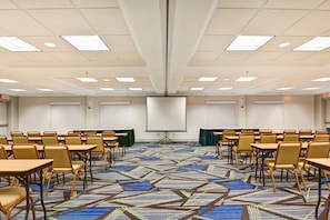 A conference room with rows of tables and chairs, a large screen, and a patterned carpet.
