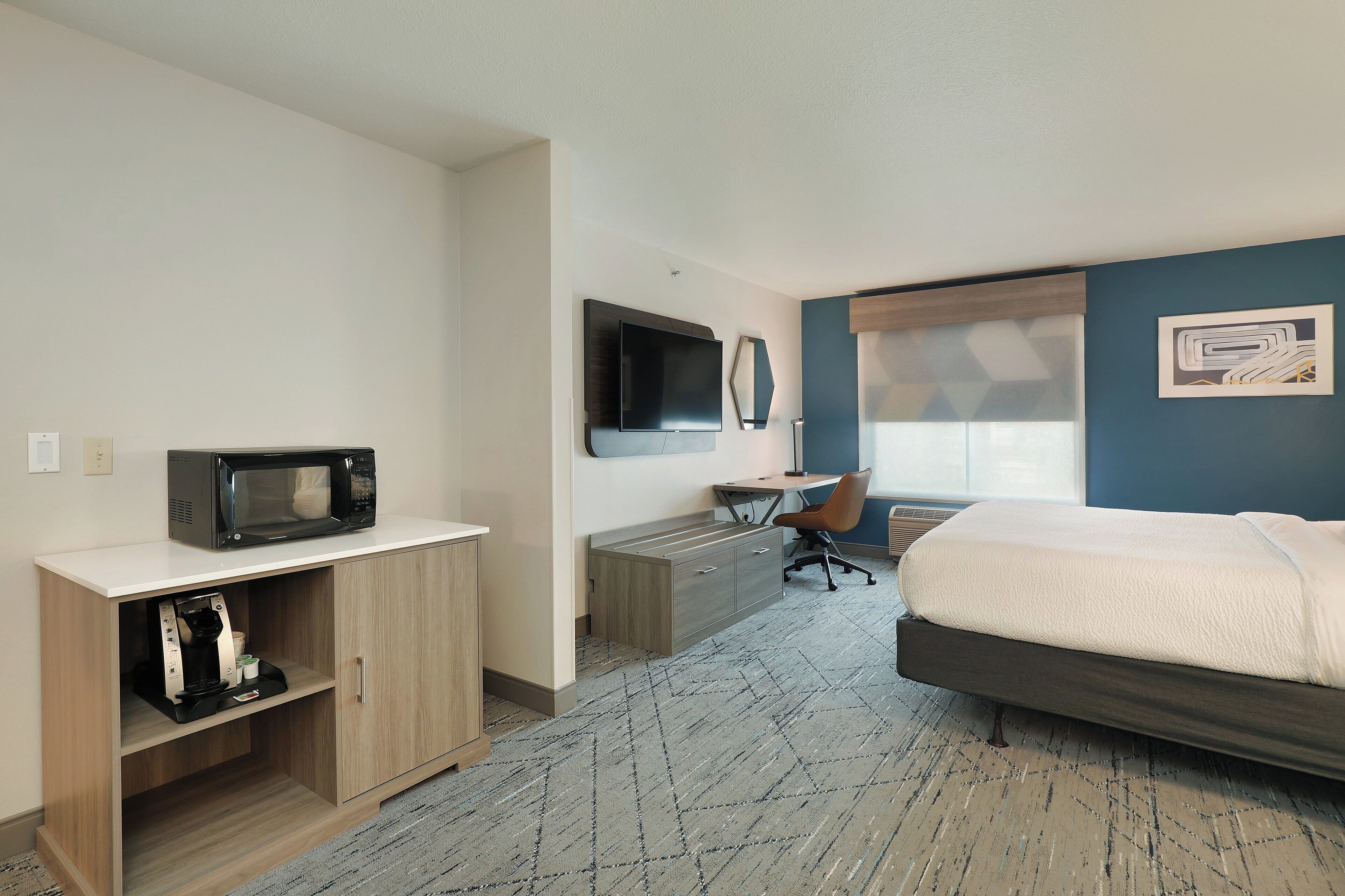 Een hotelkamer met een bed, een bureau met stoel, een magnetron, een koffiezetapparaat en een televisie aan de muur.