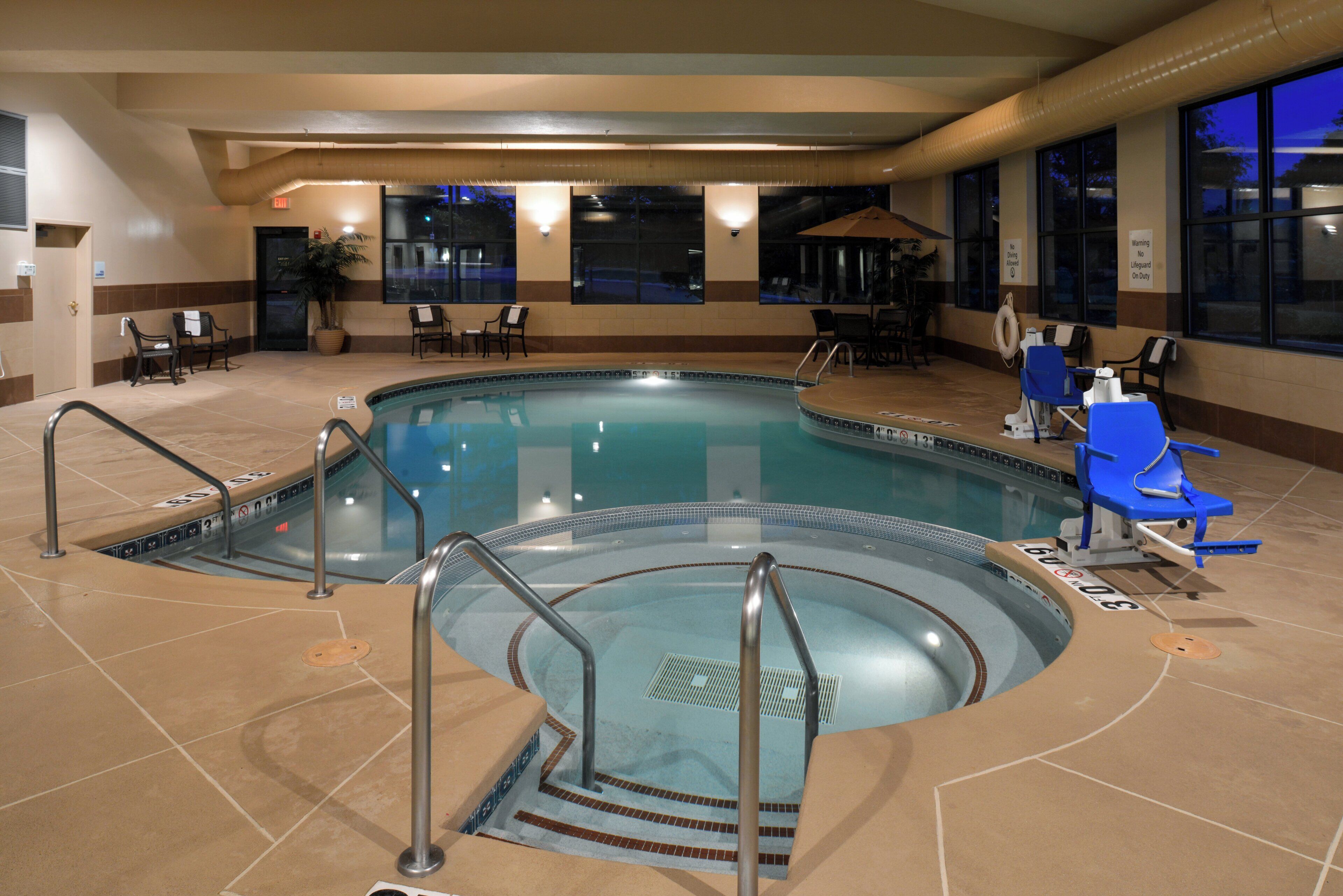 An indoor swimming pool with multiple lanes, safety railings, and lounge chairs.