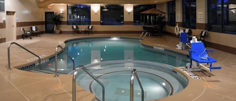 An indoor swimming pool with multiple lanes, safety railings, and lounge chairs.
