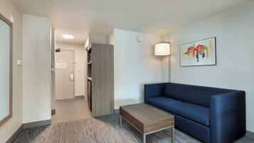 Una habitación de hotel moderna con un sofá azul, una mesa de centro de madera y una alfombra estampada.