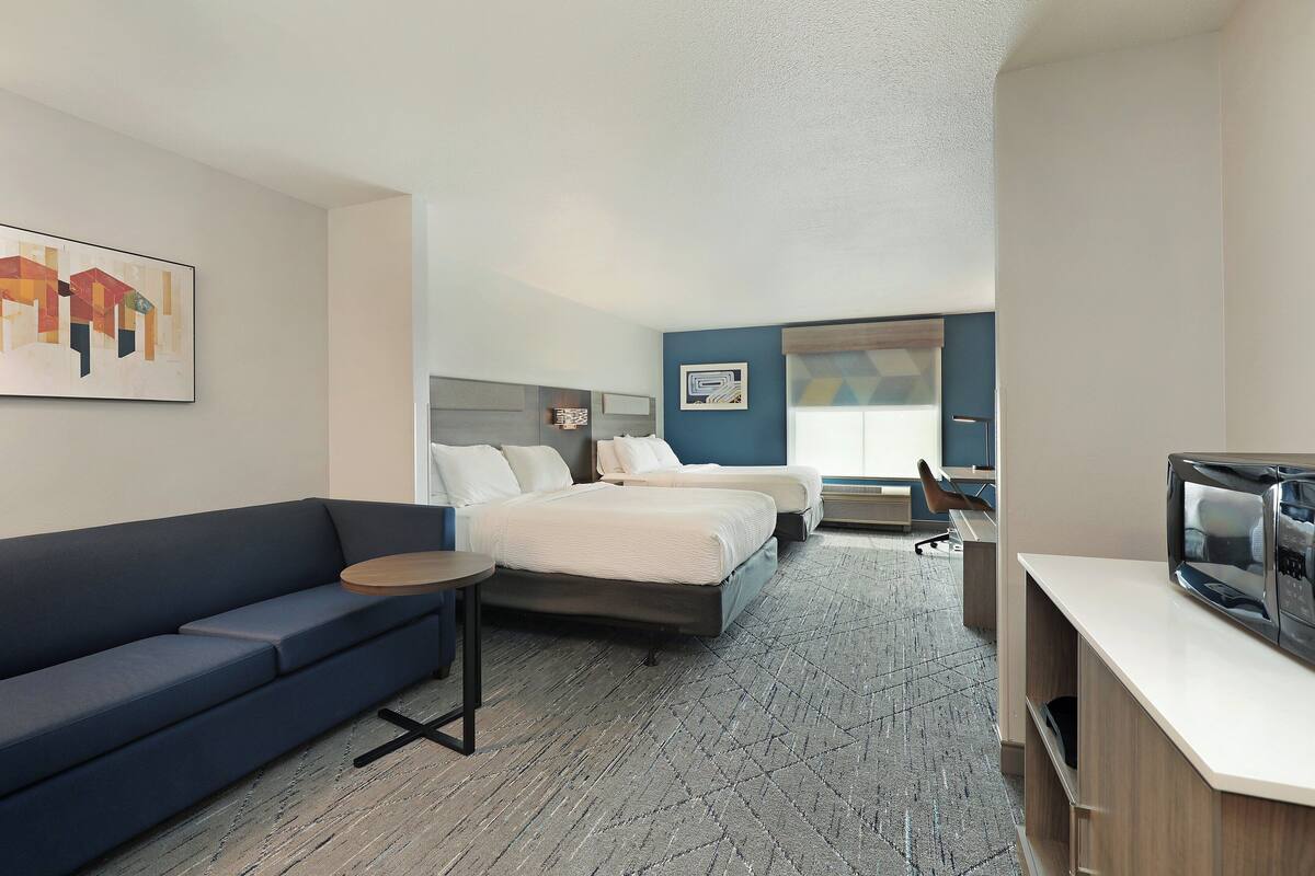 A hotel room with a sofa, a bed, a desk with a television, and a small table.