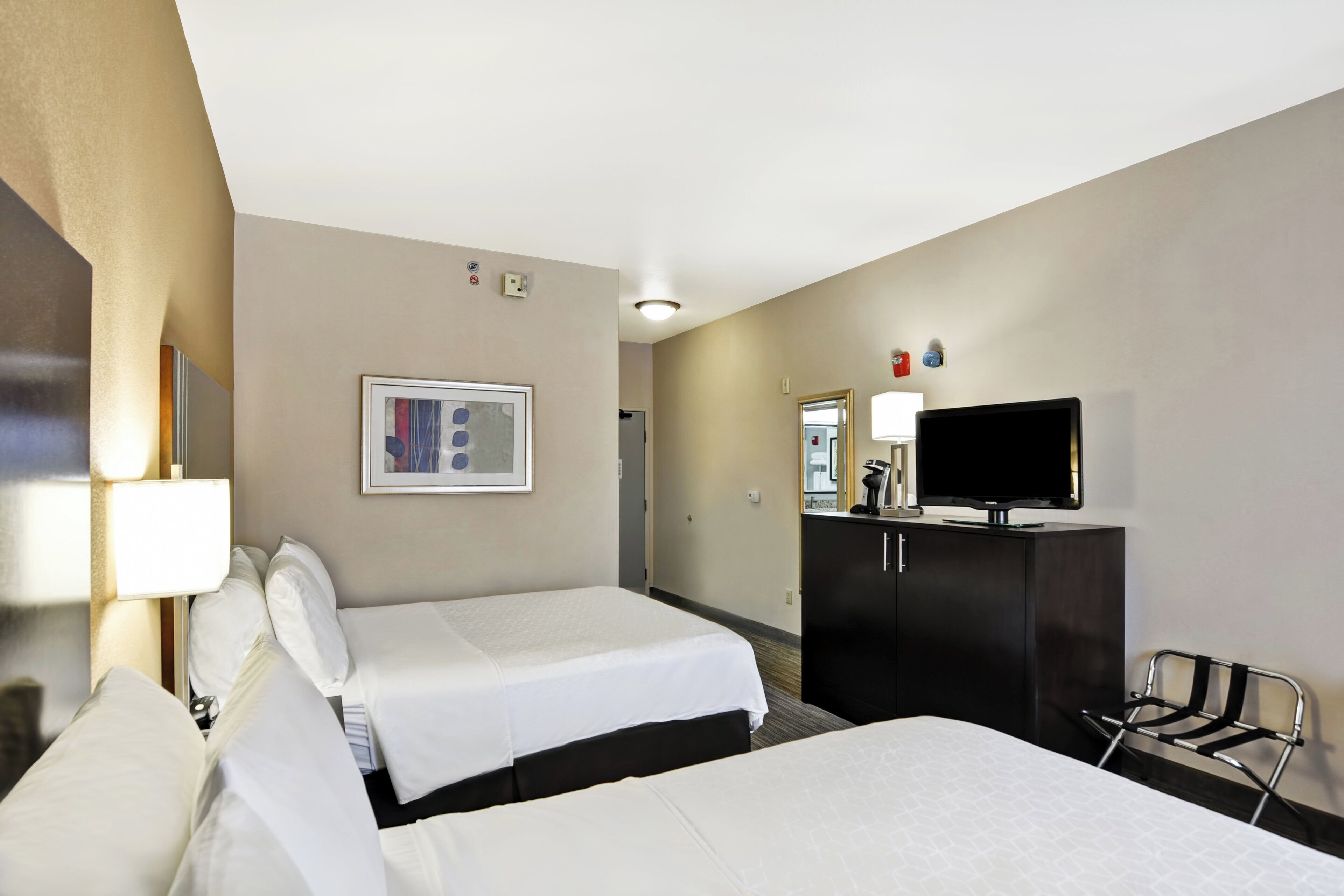 A hotel room with two beds, a television, a desk, and a chair.