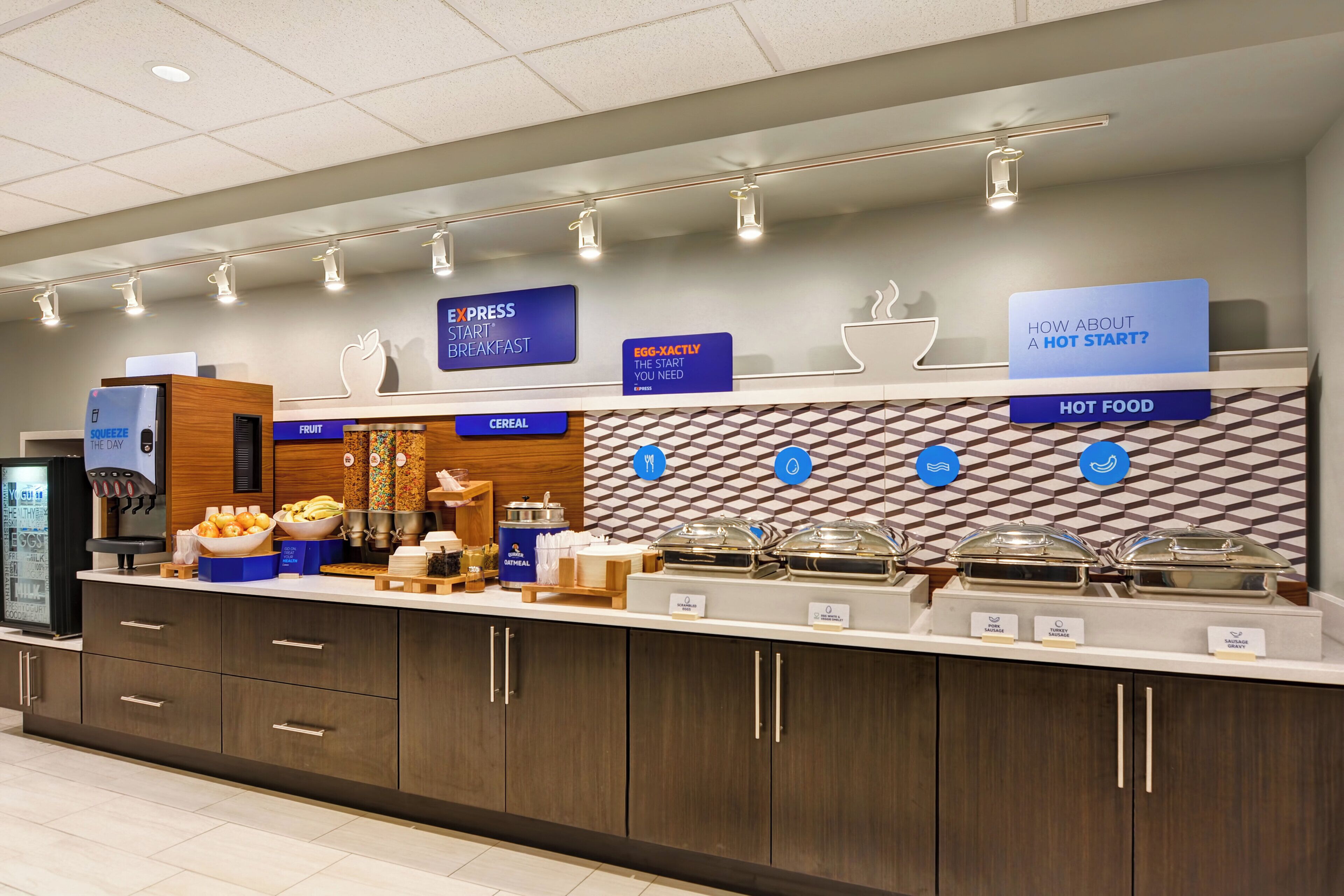 A hotel breakfast buffet with labeled food sections, a juice dispenser, and a coffee machine.