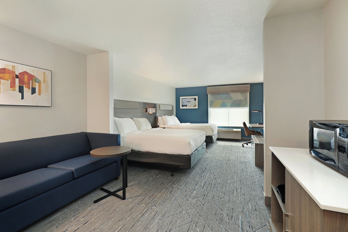 A hotel room with a sofa, a bed, a desk with a television, and a small table.