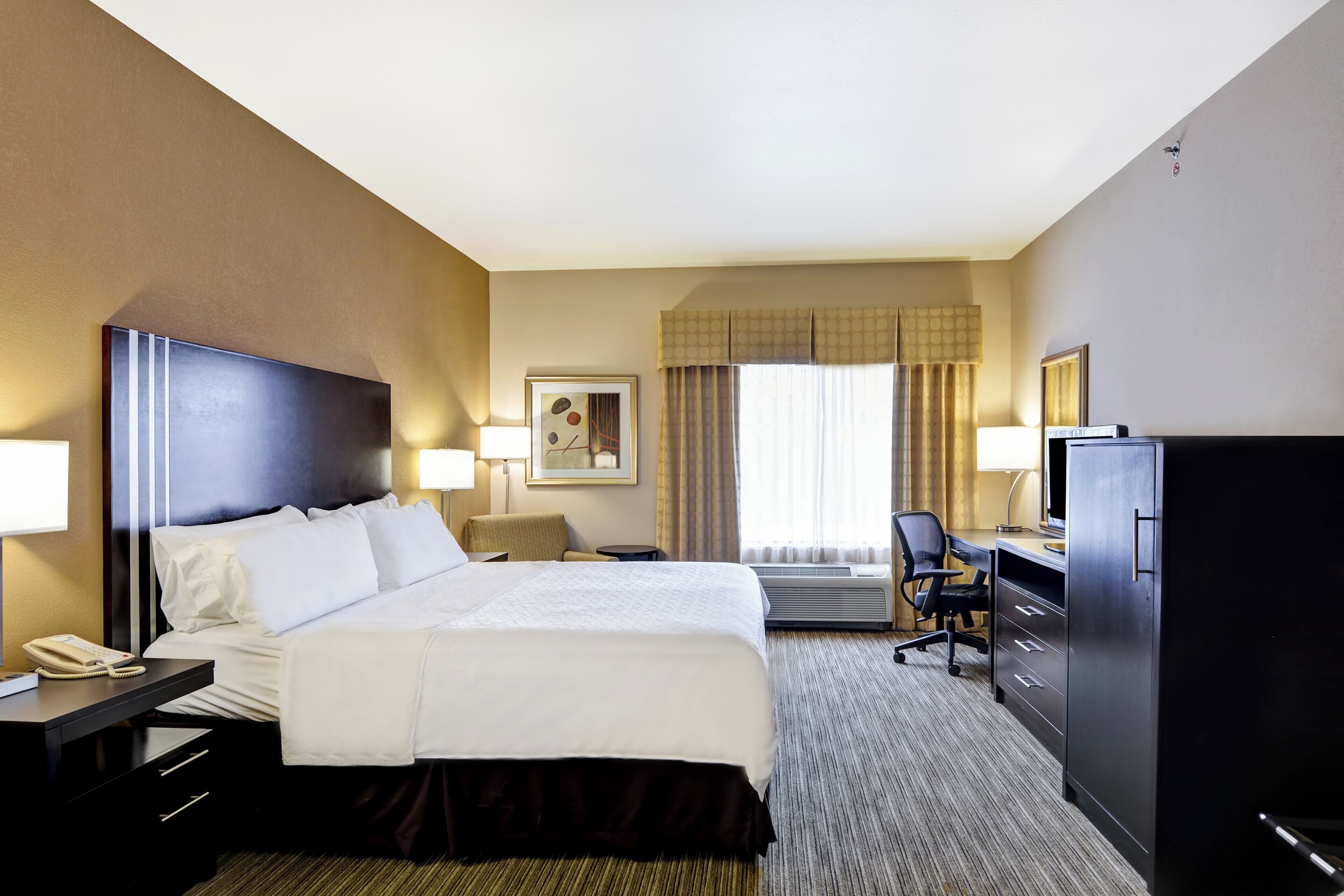 A hotel room with a large bed, a desk, a chair, a television, and a telephone.