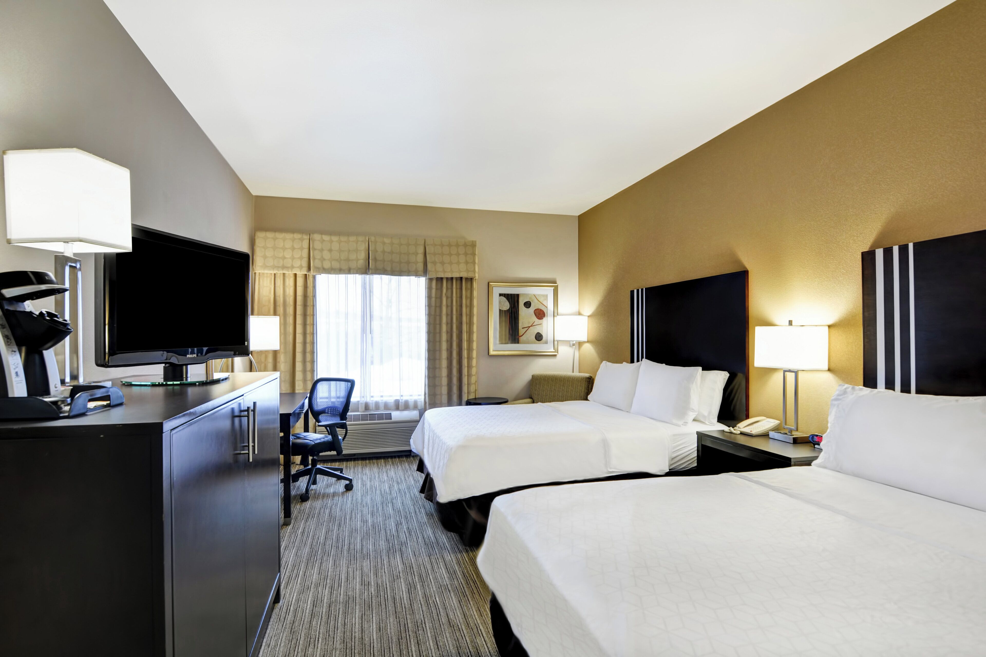 A hotel room with two beds, a desk with a television, a chair, and a desk lamp.