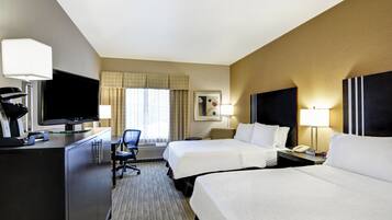 A hotel room with two beds, a desk with a television, a chair, and a desk lamp.