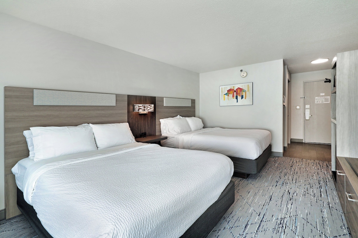 A hotel room with two beds, a wooden headboard, a wall-mounted artwork, and a patterned rug.
