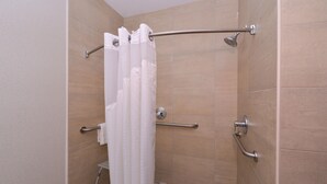 Eine Dusche mit weißer Duschkabine, Haltegriffen und einer Handbrause.