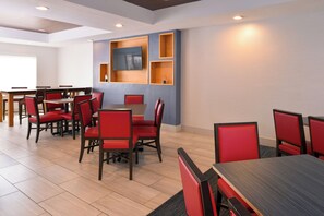 A modern dining area with multiple tables and red upholstered chairs, featuring built-in wooden shelving and recessed ceiling lighting.
