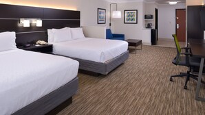 Ein Hotelzimmer mit zwei Betten, einem Schreibtisch, einem Stuhl, einem Fernseher und einem kleinen Tisch.