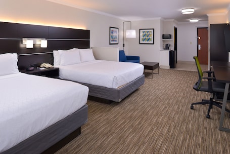 A hotel room with two beds, a desk, a chair, a TV, and a small table.