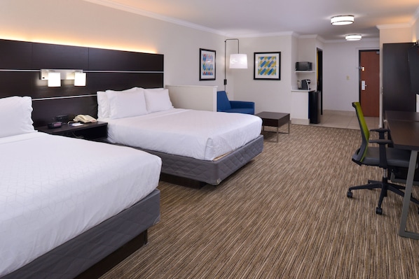 Ein Hotelzimmer mit zwei Betten, einem Schreibtisch, einem Stuhl, einem Fernseher und einem kleinen Tisch.