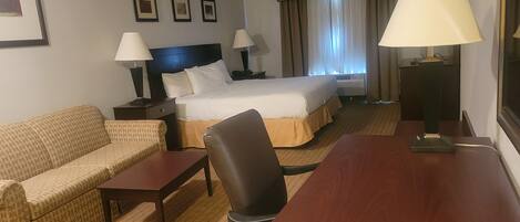 Una camera d'albergo con un letto, un divano, una scrivania e due lampade.