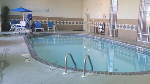 Una piscina interior con agua cristalina, suelo de baldosas y un paraguas azul.
