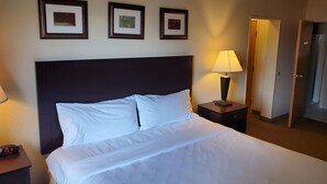 Una habitación de hotel con una cama grande, una mesita de noche con lámpara y tres cuadros enmarcados en la pared.