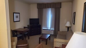 Habitación de hotel con televisión de pantalla plana, escritorio, sofá, lámpara y ventana con cortinas.