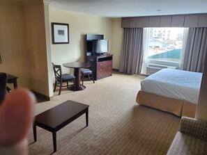 Una habitación de hotel con cama, escritorio, silla, televisor y ventana con cortinas.