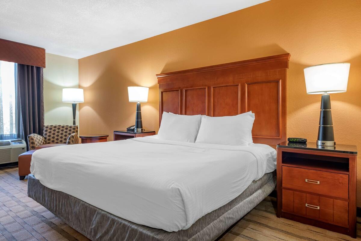 Habitación de hotel con una cama grande, dos mesitas de noche con lámparas, una silla y un reloj en la mesita.