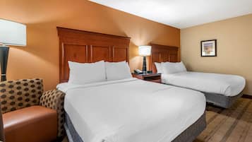 A hotel room with two beds, a wooden headboard, a nightstand, a lamp, a chair, and a framed picture on the wall.
