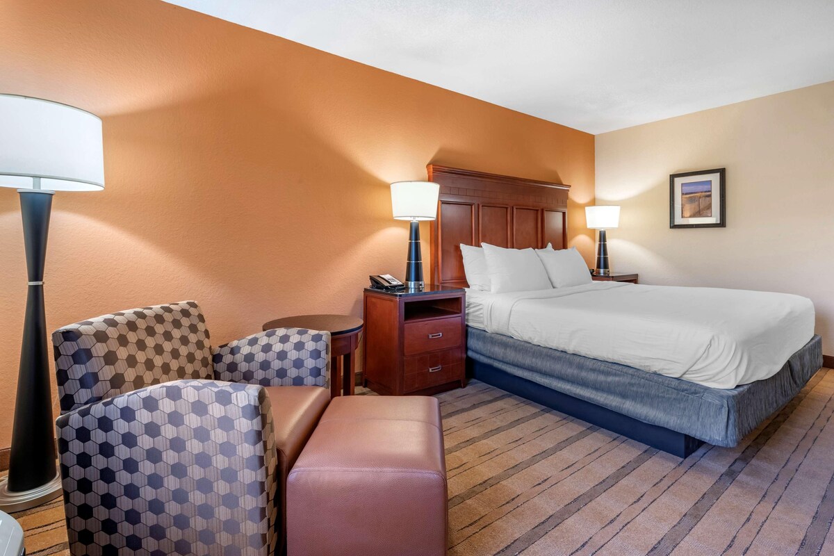 A hotel room with a bed, two bedside tables, a desk, a chair, a bench, and a lamp.
