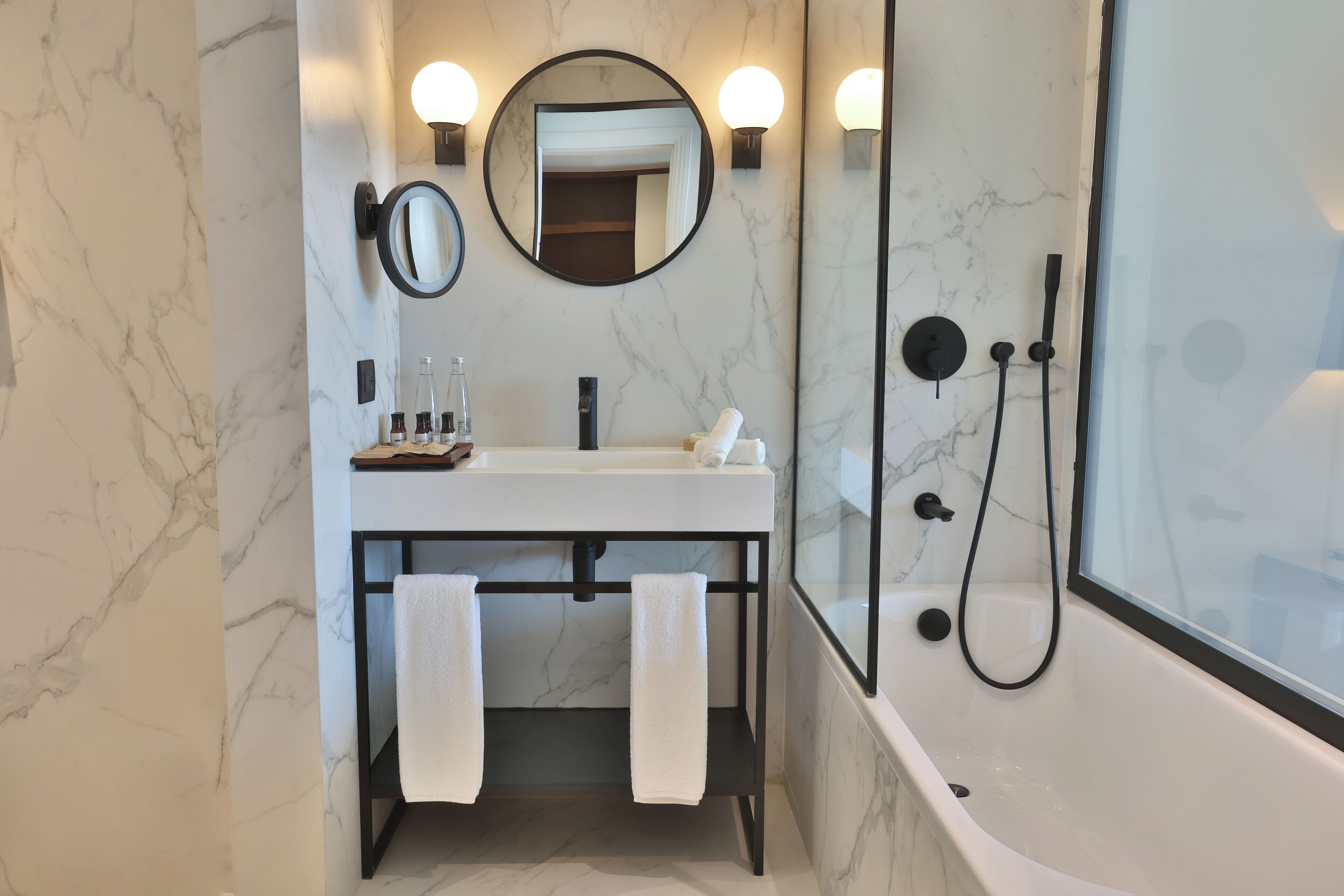 A modern bathroom with a marble wall, a sink with a mirror, and a bathtub with a showerhead.