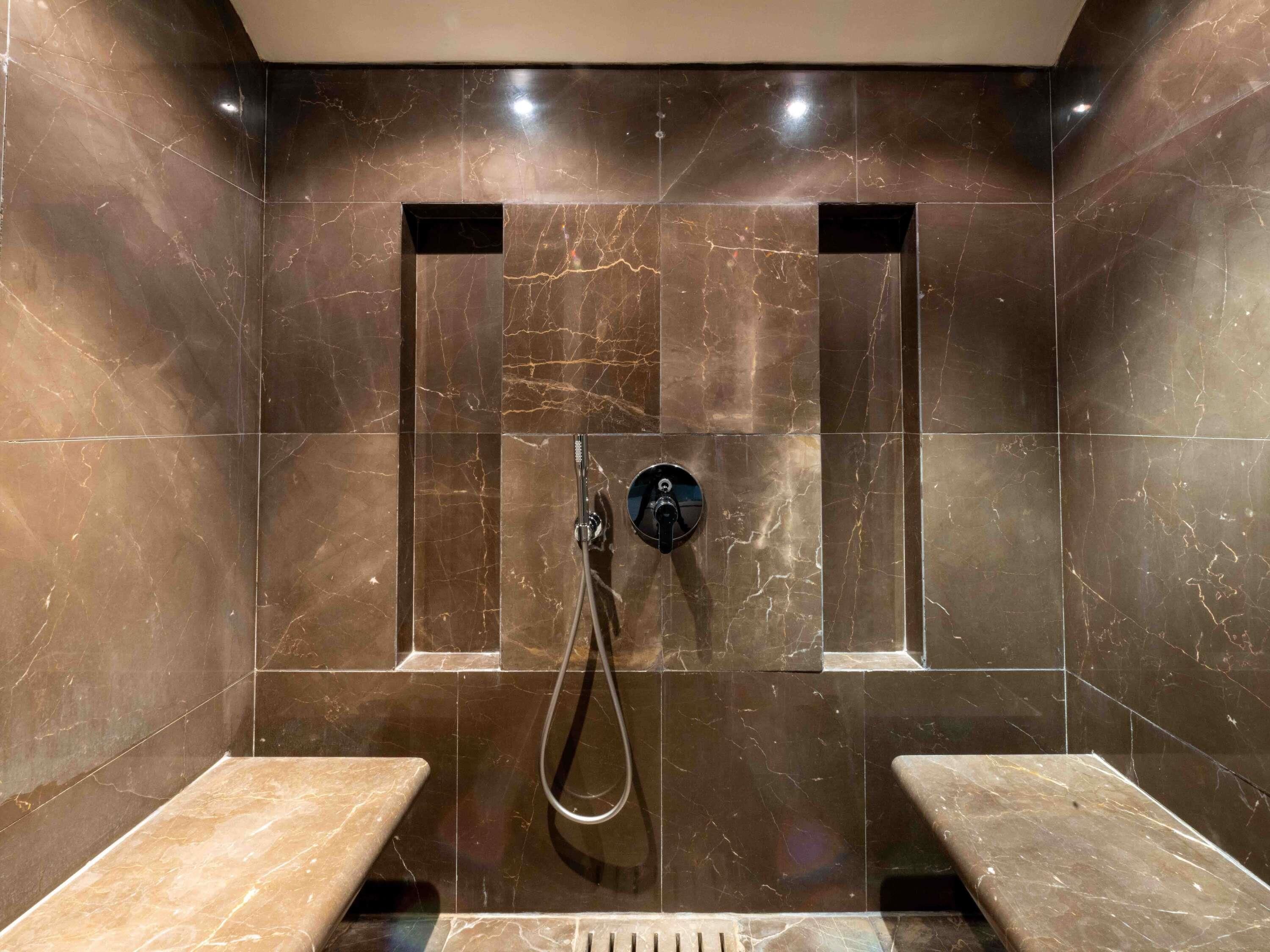 A modern shower area with marble walls and benches.