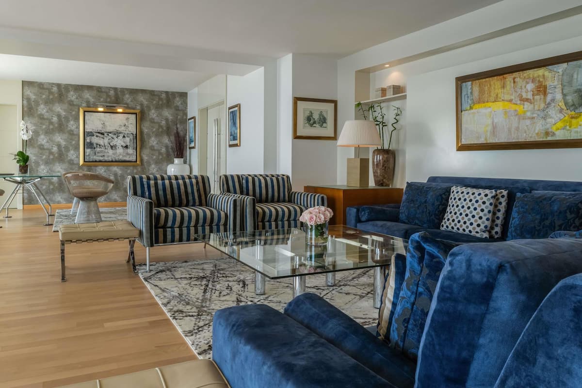 A modern living room with striped sofas, a blue velvet sofa, and a glass coffee table.